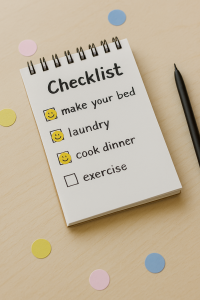 Close-up of a small notepad on a wooden desk with a checklist including ‘make your bed,’ ‘laundry,’ ‘cook dinner,’ and ‘exercise,’ with smiley face stickers next to completed tasks, surrounded by pastel stickers and a black pen.